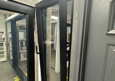 Close-up of two modern windows, one open, showing sleek black frames and a wooden surround in an indoor display setting.